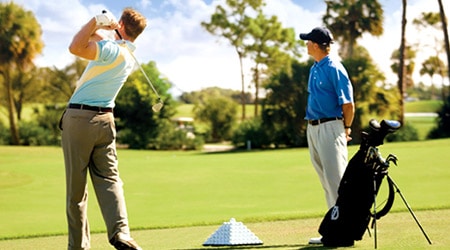 Golfer on golf course with instructor and pyramid of golf balls near propped up golf bag
